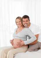 Cute pregnant woman touching her belly with her husband in the b