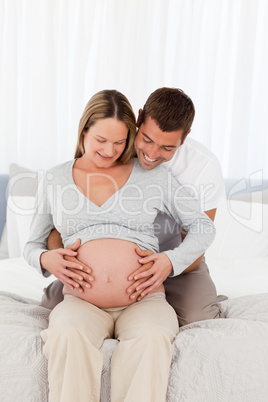 Cute future parents looking at the belly of the woman sitting on