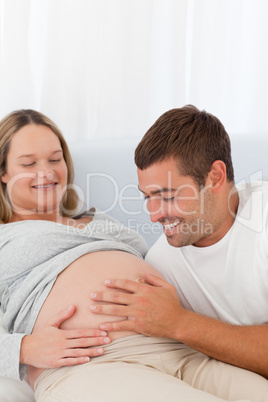 Proud future dad touching the belly of his wife lying on the bed