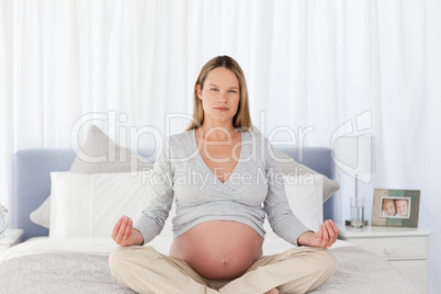 Serious future mom doing meditation on a bed