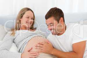 Happy future dad touching the belly of his wife while relaxing