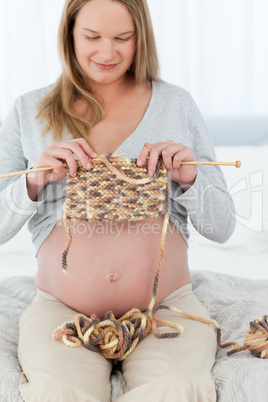 Concentrated future mom knitting sitting on a bed