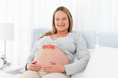 Pregnant woman resting on a bed with mom letters