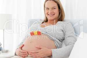 Joyful pregnant woman with mom letters on her belly while relaxi