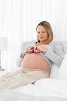 Pretty pregnant woman having  baby shoes on her belly resting on