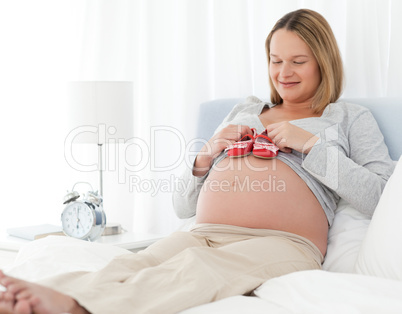 Cute pregnant woman putting baby shoes on her belly