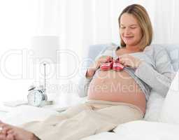 Cute pregnant woman putting baby shoes on her belly