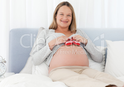 Cheerful pregnant woman putting baby shoes on her belly