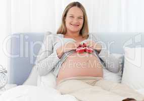 Cheerful pregnant woman putting baby shoes on her belly