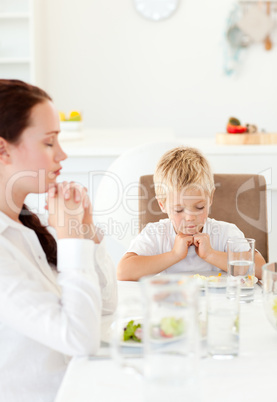 Concentrated little boy praying with his mother before eating th