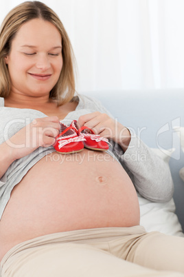 Happy future mom putting baby shoes on her belly