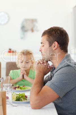 Adorable father and daughter praying during the lunch