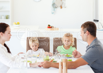 Family praying together before eating their salad for lunch