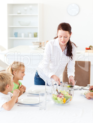 adorable mother serving salad to her children for lunch