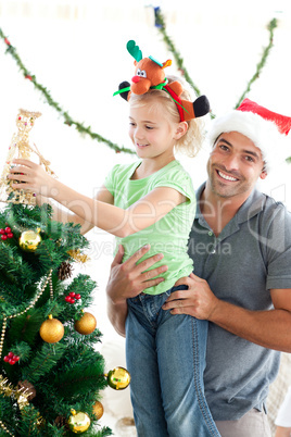 Happy father helping his daughter to put an angel on the Christm