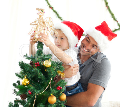Happy father helping his son to put an angel on the Christmas tr