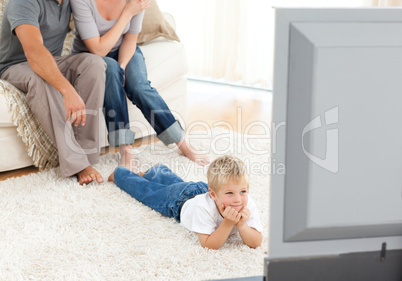 Attentive little boy watching television lying on the floor