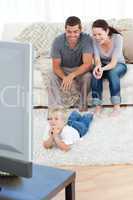 Cute little boy watching television on the floor with his parent