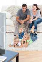 Adorable siblings watching television with their parents lying o