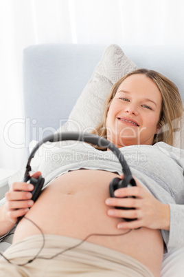 Adorable pregnant woman putting headphones on her belly