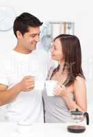 Adorable couple holding cups of coffee and looking at each other