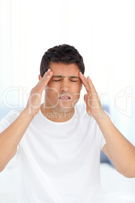 Man massaging his temples sitting on his bed