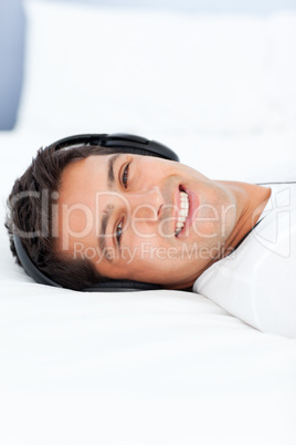 Cheerful man listening music with headphones lying on his bed