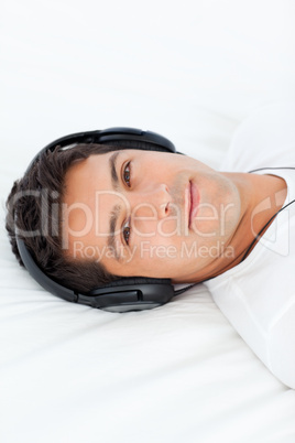 Serious man with headphones on lying on his bed