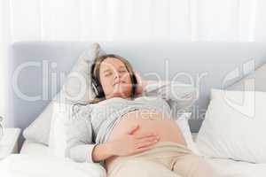 Relaxed future mom listening to the music on a bed