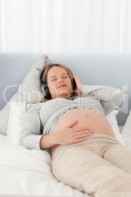 Peaceful future mother with headphones on lying on a bed