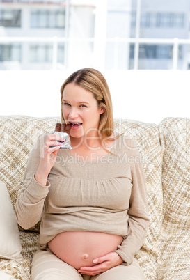 Pretty future mom eating a chocolate bar sitting on the sofa