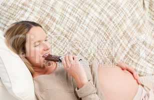 Adorable prgnant woman devouring a chocolate bar while relaxing