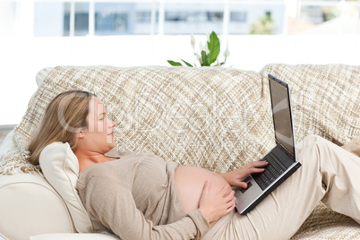 Smiling pregnant woman using her laptop lying on the sofa