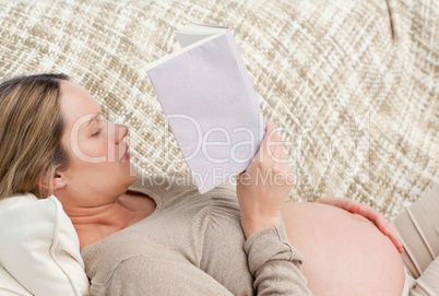 Cute future mom reading a book while relaxing on the sofa