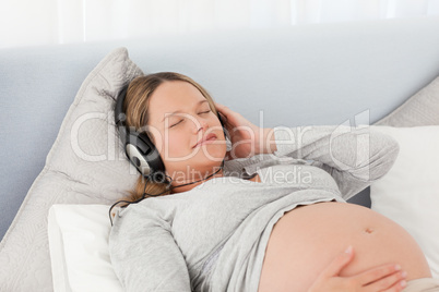 Pretty future mom listening to the music lying on a bed