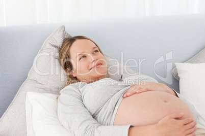 Thoughtful pregnant woman resting on a bed