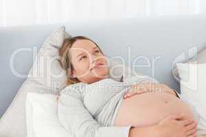 Thoughtful pregnant woman resting on a bed