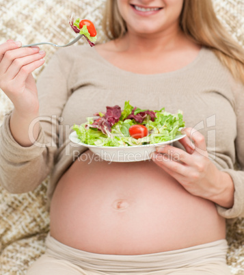 Close up of a future mom eating a salad sitting in the living ro