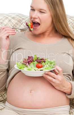 Cute pregnant woman eating a salad sitting on the sofa