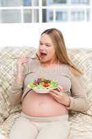 Pregnant woman devouring a salad in the sofa