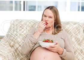 Funny future mom eating strawberries resting on the sofa