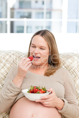 Hungry pregnant woman eating strawberries sitting in the living-