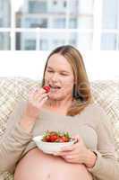 Hungry pregnant woman eating strawberries sitting in the living-