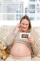 Happy pregnant woman looking at an echography while phoning