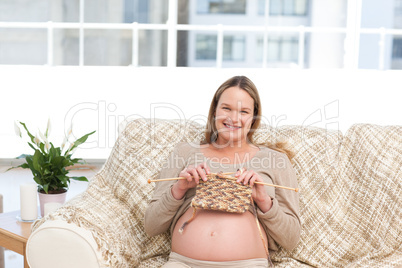 Pretty woman knitting for her future baby sitting on the sofa