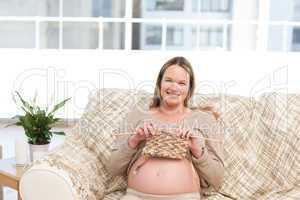 Pretty woman knitting for her future baby sitting on the sofa