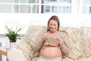 Happy pregnant woman knitting in the living-room