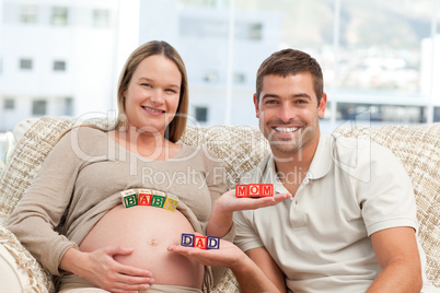 Happy future parents holding cubes sitting in the sofa