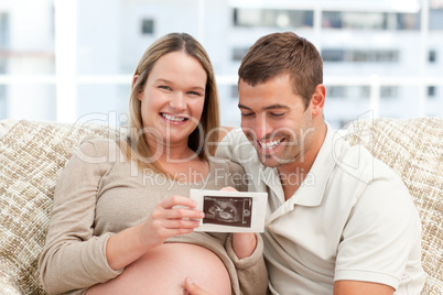 Beautiful pregnant woman showing her echography to her husband