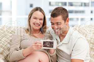 Beautiful pregnant woman showing her echography to her husband